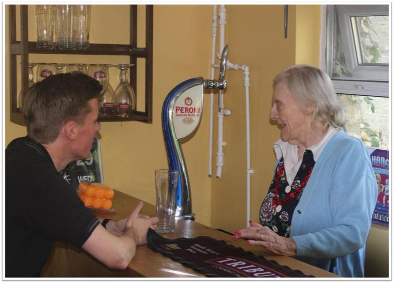 an older lady behind a bar talking to a younger man