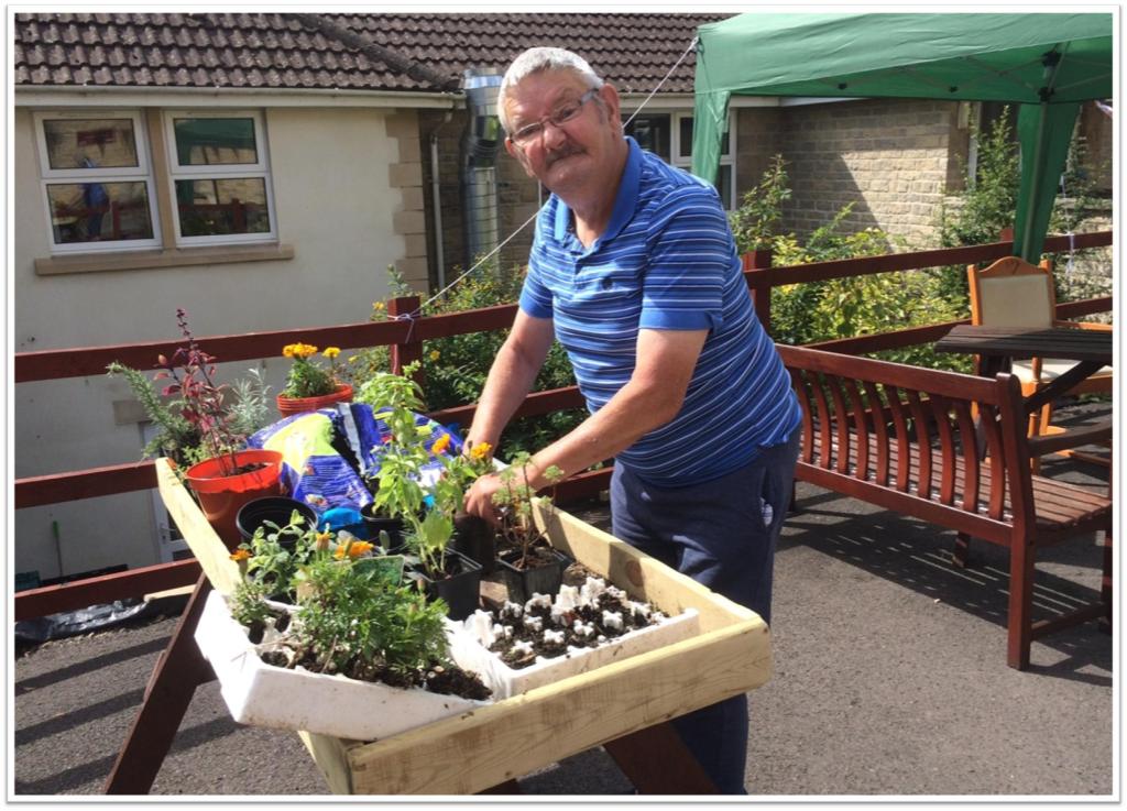 an elder man stood tending to some plants in a table outside