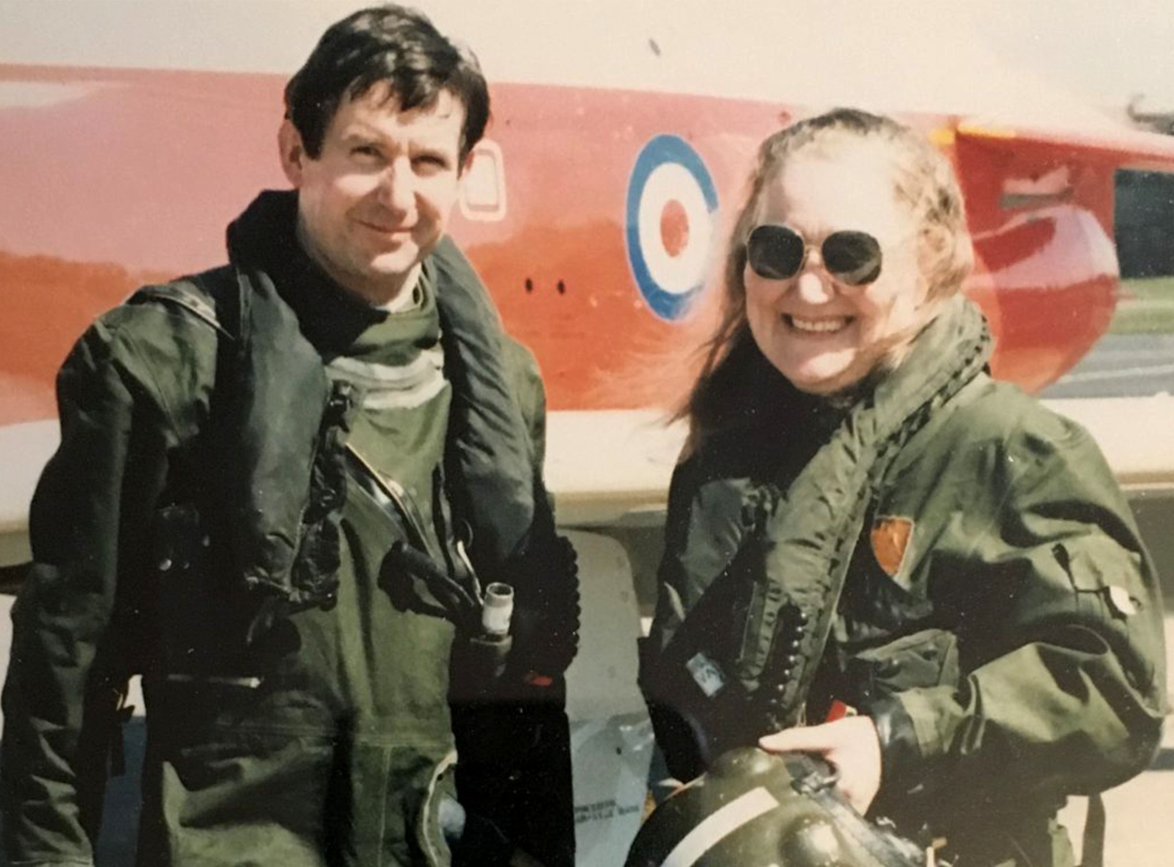 a man and a woman wearing aircraft suits with a plane behind them