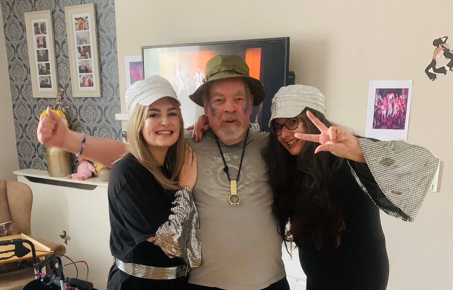 an elderly man with a green hat standing with two women in each arm