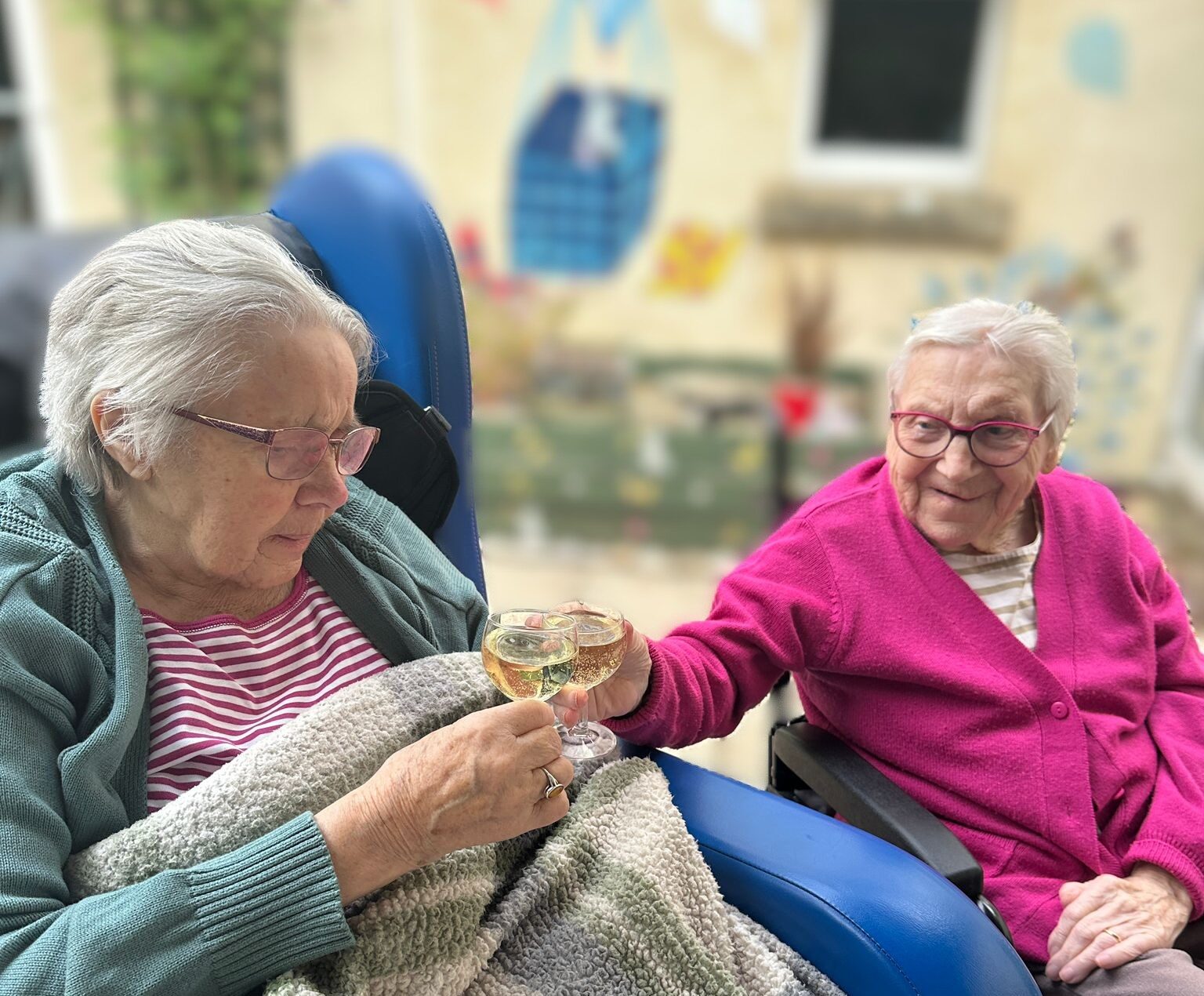 Two older women sit together enjoying a drink outside, while another family member smiles as she sips fizz from a glass.